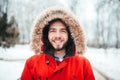 Portrait, close-up of a young stylishly dressed man smiling with a beard dressed in a red winter jacket with a hood and fur on his Royalty Free Stock Photo