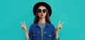 Portrait close up young woman blowing her red lips sending sweet air kiss wearing a black round hat, denim jacket on a blue Royalty Free Stock Photo