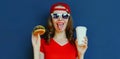 Portrait close up of young woman with burger and coffee cup wearing baseball cap, sunglasses over blue Royalty Free Stock Photo