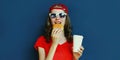 Portrait close up of young woman with burger and coffee cup wearing baseball cap, sunglasses over blue Royalty Free Stock Photo