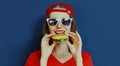 Portrait close up of young woman eating burger wearing baseball cap, sunglasses over blue Royalty Free Stock Photo