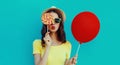 close up of young woman with lollipop and red balloon blowing a red lips wearing a summer straw hat on a blue background Royalty Free Stock Photo