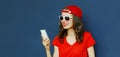 Portrait close up of young woman with phone wearing a red baseball cap over blue Royalty Free Stock Photo