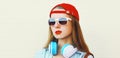 Portrait close up of young woman in red baseball cap and wireless headphones listening to music over white background Royalty Free Stock Photo