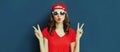 Portrait close up of young woman showing peace sign gesture wearing baseball cap over blue Royalty Free Stock Photo