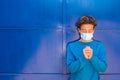 Portrait and closeup of man teenager praying and wearing medical and surgical mask on his face - millennial praying with closed
