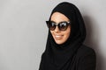 Portrait closeup of muslim fashion woman 20s in religious headscarf and sunglasses smiling and looking aside, isolated over gray Royalty Free Stock Photo