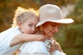 Portrait closeup of pretty curly little girl with love embracing mother in hat holding bouquet of wildflowers. Mom and Royalty Free Stock Photo