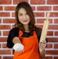 Portrait closeup shot of Asian pastry chef in orange apron standing smiling look at camera showing wooden roller and mixing dough Royalty Free Stock Photo