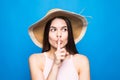 Portrait closeup of woman wearing straw hat showing finger at lips to keep secret isolated over blue background Royalty Free Stock Photo