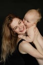 Portrait closeup of young smiling mother holding and embracing cute naked baby on black background. Happy parent