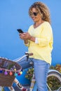 Portrait of coloured style trendy look cheerful yong adult womam use cellular phone sitting on a vintage trendy bike - yellow and