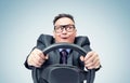 Portrait of a comical businessman in a dark suit and glasses holding a car steering wheel in his hands, on a blue background