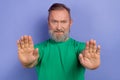 Portrait of concentrated aged person raise arms palms demonstrate stop symbol isolated on purple color background