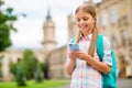 Portrait of concentrated small girl using device holding rucksack backpack wearing checkered plaid t-shirt standing