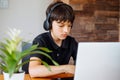 Portrait of concentrated teenager boy wearing black T-shirt, headphones sitting at desk, using laptop, surfing internet. Royalty Free Stock Photo