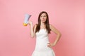 Portrait of Concerned puzzled bride woman in white lace wedding dress standing and holding megaphone on pink