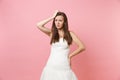 Portrait of concerned puzzled bride woman in white wedding dress stand have problem keeping hand on head isolated on