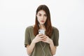 Portrait of concerned worried smart woman in casual outfit, holding smartphone and listening music in earphones, biting