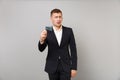 Portrait of concerned young business man in classic black suit and shirt holding credit bank card isolated on grey