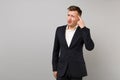 Portrait of concerned young business man in classic black suit and shirt holding finger on temple isolated on grey