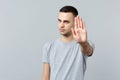 Portrait of concerned young man in casual clothes looking camera, showing stop gesture with palm isolated on grey Royalty Free Stock Photo