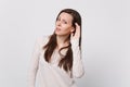 Portrait of concerned young woman in light clothes looking camera and eavesdrop with hearing gesture on white