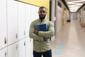 Portrait of confident african american young male teacher with files standing in school corridor Royalty Free Stock Photo