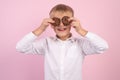 Portrait of confident attractive little boy holds american chocolate chip cookies on the eyse, dressed white stylish shirt