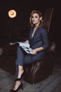 Portrait of a confident beautiful business woman in a suit on a dark background with a magazine in her hands. The concept of Royalty Free Stock Photo