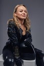 Fashion, sport, extreme. Portrait of a confident biker girl wearing racer costume sitting on a gray box in a studio. Royalty Free Stock Photo