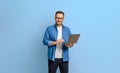 Portrait of confident businessman doing online research over laptop against blue background