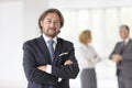 Portrait of confident businessman standing with arms crossed against colleagues at office Royalty Free Stock Photo