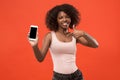 Portrait of a confident casual afro girl showing blank screen mobile phone isolated over red background Royalty Free Stock Photo