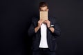 Portrait of confident concentrated self-assured handsome bearded guy covers his face with a notebook, isolated on black background