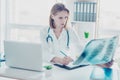 Portrait of confident concentrated smart doctor looking at x-ray photo of ill patient and writing down the diagnose to the record Royalty Free Stock Photo