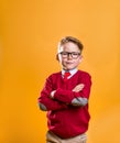 Portrait of confident cute seven years old kid boy on yellow background. Pupil in business school uniform and glasses