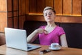 Portrait of confident egoist young girl with short hair in pink t-shirt and eyeglasses is sitting alone in cafe and pointing