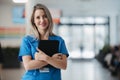 Portrait of confident female doctor in hospital corridor. Beautiful nurse wearing blue uniform, holding clipboard Royalty Free Stock Photo