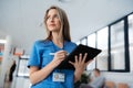 Portrait of confident female doctor standing in Hospital corridor. Beautiful nurse wearing blue scrubs, holding