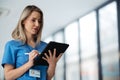 Portrait of confident female doctor standing in hospital corridor. Beautiful nurse wearing blue scrubs, holding Royalty Free Stock Photo