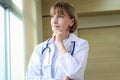 Portrait of confident female doctor in workwear with stethoscope thinking and taking decisions with hand on chin, looking through