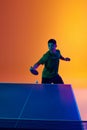 Portrait of confident and focused on game Asian table tennis player neon light against warm yellow gradient background