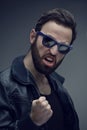 Portrait of a bearded man in sunglasses and leather jacket, shows the gesture clenched fist, over grey background. Royalty Free Stock Photo