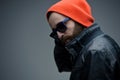 Portrait of a bearded brutal man in sunglasses and orange hat and black leather jacket, isolated on a grey background. Royalty Free Stock Photo