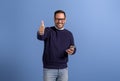 Portrait of confident happy businessman with mobile phone gesturing thumbs up on blue background Royalty Free Stock Photo