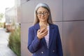 Portrait of a confident mature business woman in classic wear using smartphone while standing outdoors. Checking email Royalty Free Stock Photo