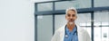 Portrait of confident mature doctor standing in hospital corridor. Banner of handsome doctor with gray hair wearing Royalty Free Stock Photo