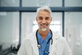 Portrait of confident mature doctor standing in Hospital corridor. Handsome doctor with gray hair wearing white coat Royalty Free Stock Photo