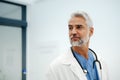 Portrait of confident mature doctor standing in Hospital corridor. Handsome doctor with gray hair wearing white coat Royalty Free Stock Photo